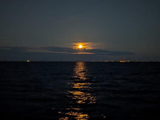 Yellow moon rising above the clouds and being reflected in the water.