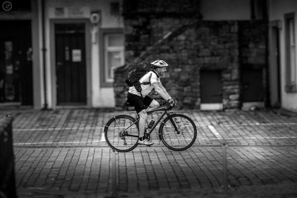 monochrome shot of man on cycle with backdrop of old buildings