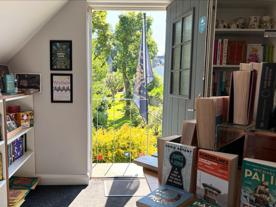 A view from inside the Wedale Bookshop through an open door, looking out into a beautiful garden with trees and bushes.
