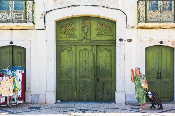 A woman carries a shopping trolley while fanning herself as she walks past a green garage door.