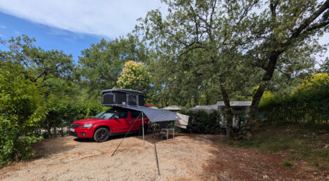 Ein Auto mit einem Dachzelt und einem am Auto befestigten tarp auf einer gesplitteten Campingplatzparzelle.