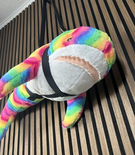 rainbow colored plush shark in a fancy carrying harness
