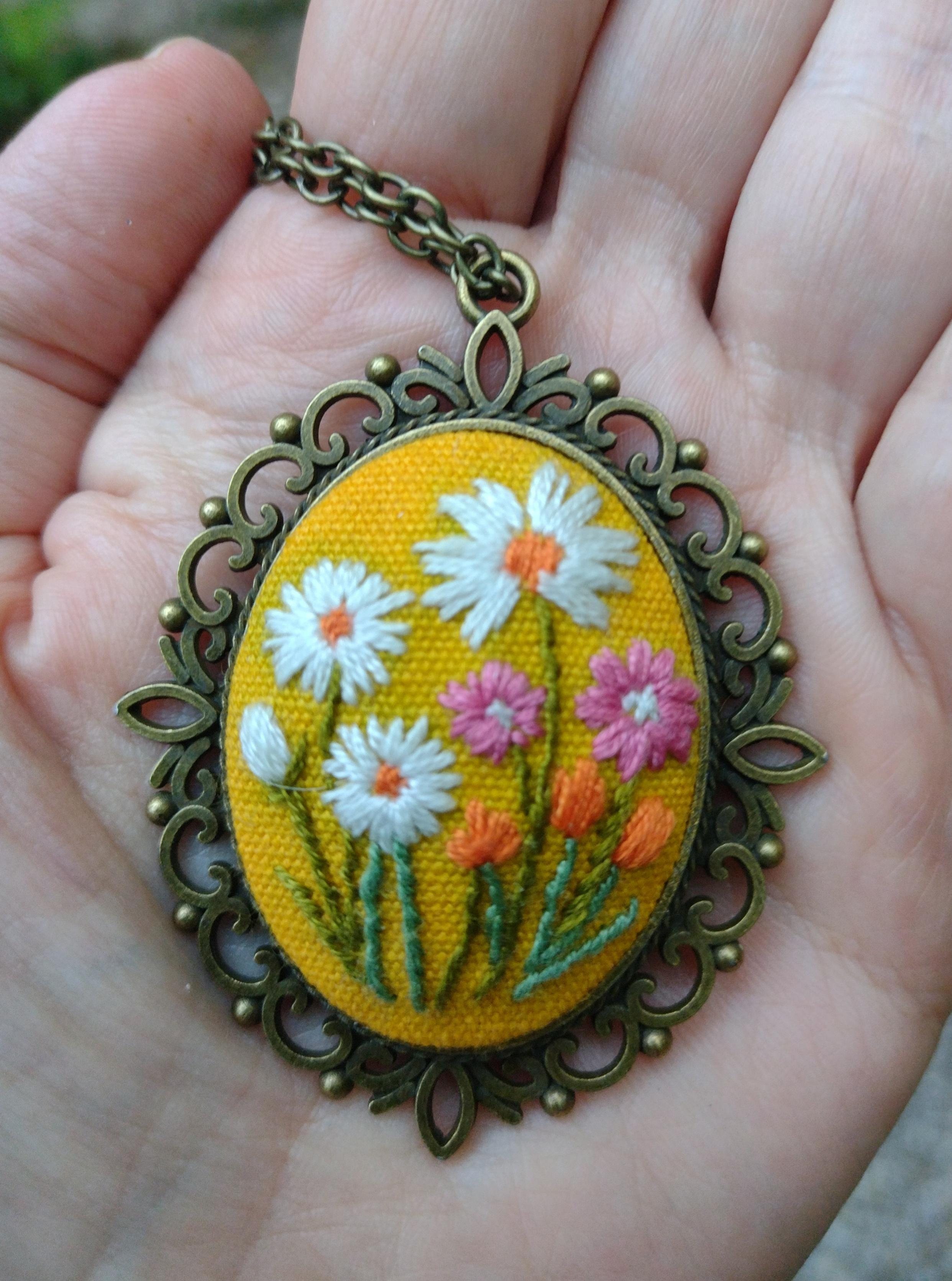 Photo of a pendant embroidered with various flowers, on a chain, lying on my hand.