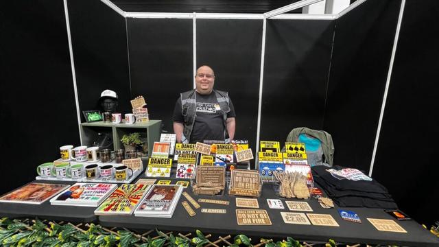 Me, standing behind a stall loaded with wood and metal signs, coasters, mugs, and other items.
