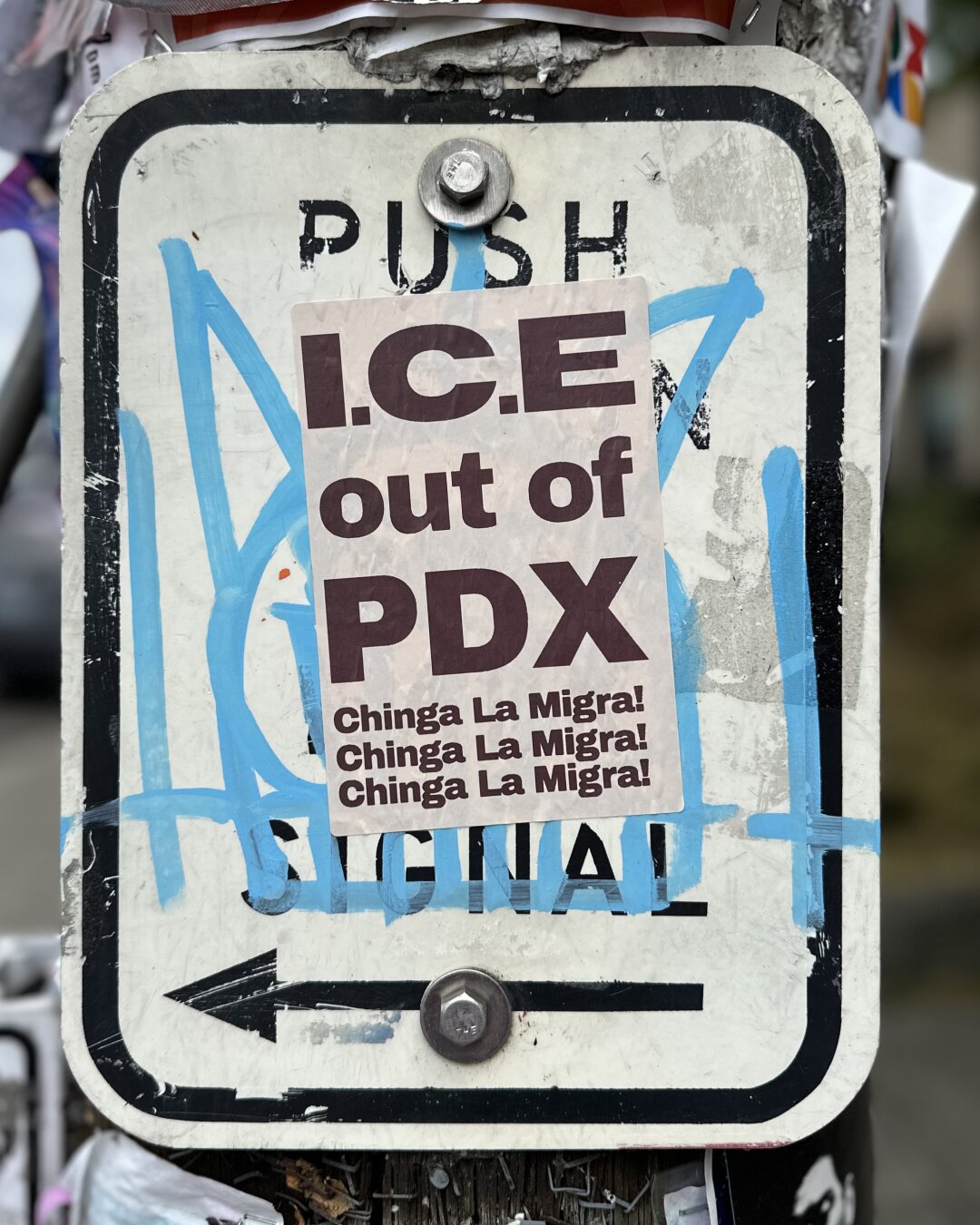 A sticker placed below the “Push” of a “Push to walk” sign reads, “ICE out of PDX. Ching la migra”