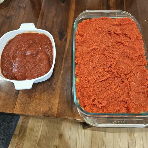 A casserole covered with tomato sauce on the left, and a larger casserole covered with nomato sauce on the right. The nomato sauce is a brighter, orangier red, but is still definitely red.