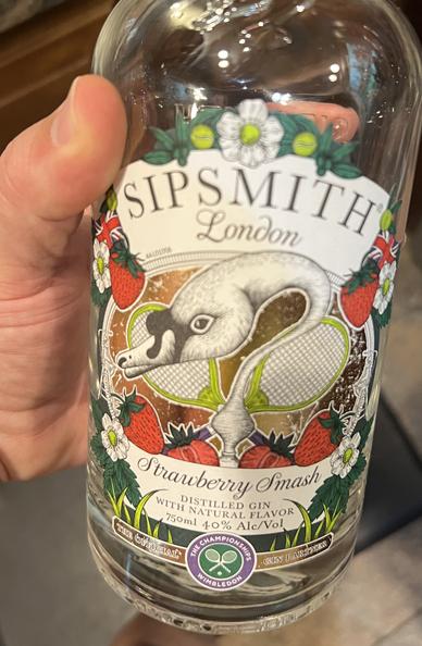 Photo of my hand holding a recently emptied bottle. It says sip smith London at the top. It has a white goose drawing in the center of the label with strawberries in the border. And then calligraphic letters saying “Strawberry Smash”.