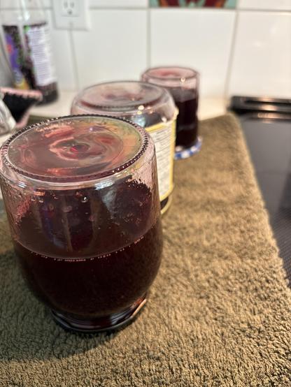 Three jars with a dark red liquid are standing upside down on a green towel