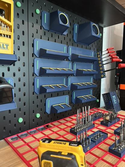 The same 3D printed Gridfinity baseplates are hanging from the SKÅDIS pegboard.  Now the bins are on the shelf below.  The empty baseplates have magnets in the corners of each grid unit, and gold highlights around the perimeter.
