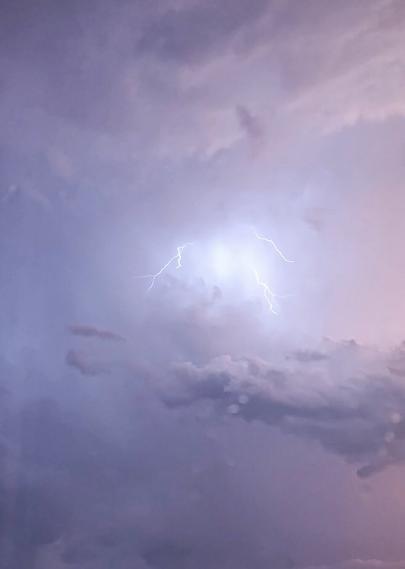 Picture of a sky full of storm clouds. Above the biggest cloud in the middle of the photo there is big lightning branching in different directions. Sky is light colored and it has some light pink hues.