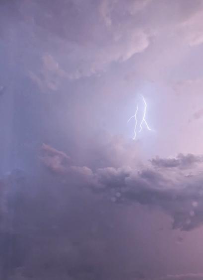 Picture of a sky full of storm clouds. Above the biggest cloud there is two vertical lightnings right next to each other. Sky is light colored and it has some light pink hues.