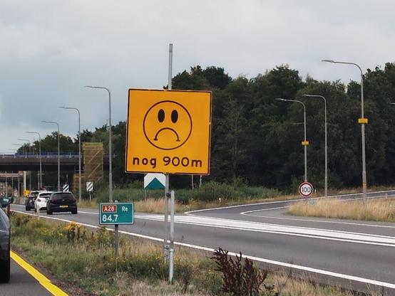 Yellow (meaning temporary) traffic sign containing a sad smiley and the text "nog 900m".