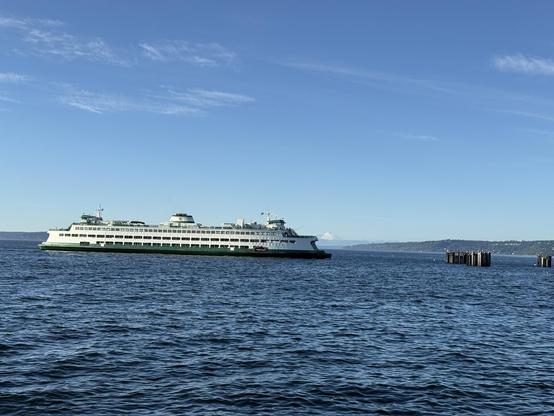 Ferry docking with Mount Baker in the background. Old pier on the right with a blue sky overhead.