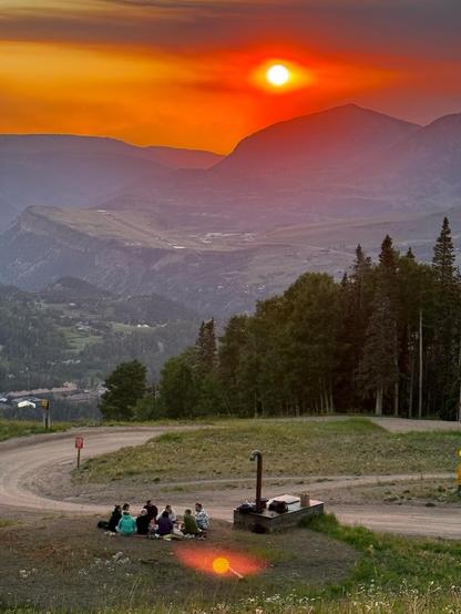 Nine neuromorphic engineers sit in a circle on a blanket, while having a picnic dinner on mountain above Telluride Colorado. The setting sun gives off an intense red glow.
Photo credit: Guido Zarrella