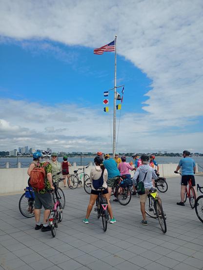 People standing by their bicycles. Flag pole with the American flag, blue shy.