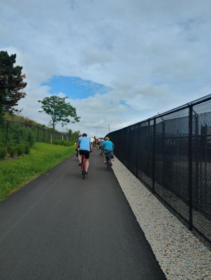 Bike path, riders ahead, grass on the left, fence on the right
