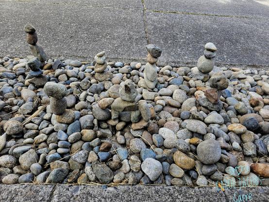 Eight small cairns grace a sidewalk strip of cobblestones next to the street. They are just three or four stones piked on each other spread out over about 2 meters of strip. The cobblestones are mostly oblong, rounded, and in varying shades of gray.