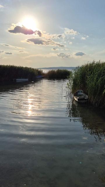 A photo of lake Balaton with boats and the sun half covered by a cloud
