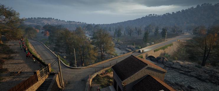 A top-down, wide shot captures a rally car racing across an old stone bridge over a river, surrounded by a lush, forested valley under a cloudy sky. The car, a bright white blur, is mid-action on a dirt road that winds through the natural landscape. To the left, another road curves upwards, lined with spectators. A building with a red-tiled roof is visible in the foreground, blending into the scene.