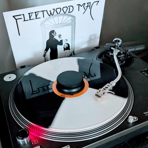 A record plays on a turntable. A record sleeve with the words "Fleetwood Mac" on it is in the background.