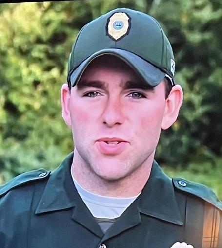 A man wearing a green baseball cap and green uniform speaks to the camera.