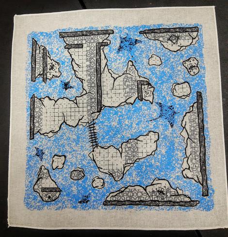 A square cotton map printed in black, grey, and blue. Map depicts the remnants of a stone floor decorated in grey and surrounded by tumultuous water. Beneath the waves, you can make out the silhouettes of two large and three small manta rays weaving around the remaining structures
