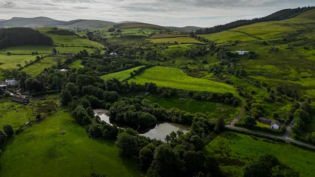 Aerial shot over wood covered pool, with farmland stretching into distant mountains