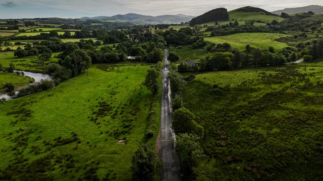 Aerial shot over straight country road, with farmland stretching into distant mountains