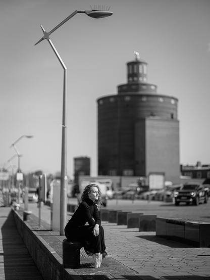 Balletttänzerin in urbaner Umgebung auf einem Hafenpoller sitzend, die Füße in Spitzenstellung.