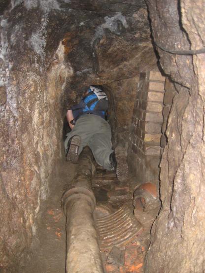 Ein Mensch kriecht durch einen ziemlich engen Tunnel. Der Mensch passt mit Rucksack gerade so hinein