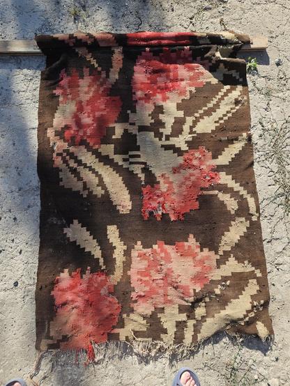 A torn ff piece of area rug that, with many holes, discolored, and with color bleeds. It used to be black background with really large red carnations