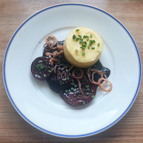 Das fertige Gericht auf dem Teller. Das Püree in einem Ring angerichtet, 4 Scheiben Kohlrabi mit einer sehr dunklen Sauce, darauf Zwiebelringe + Schnittlauch