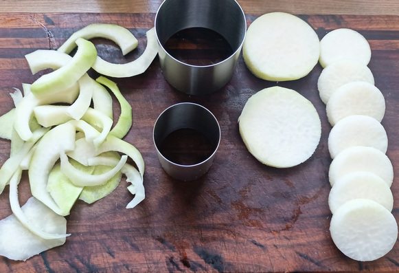 Rechts 2 große + 7 kleine Scheiben Kohlrabi, in der Mitte ein größerer + ein kleinerer Servierring, mit dem sie ausgestochen wurde, links die Reste vom Kohlrabi.