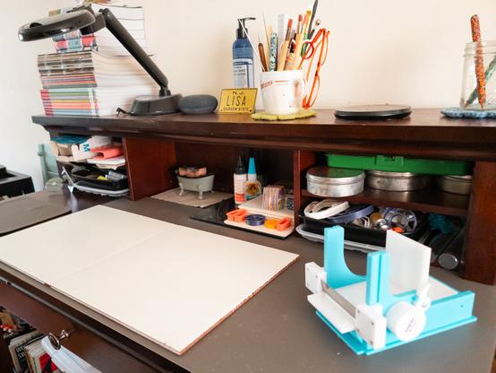A freshly-cleaned-up work area, with two square feet of empty workspace to the left, and a polymer clay millefiori cane slicer to the right. At the back of the desk are various tools I use for working.