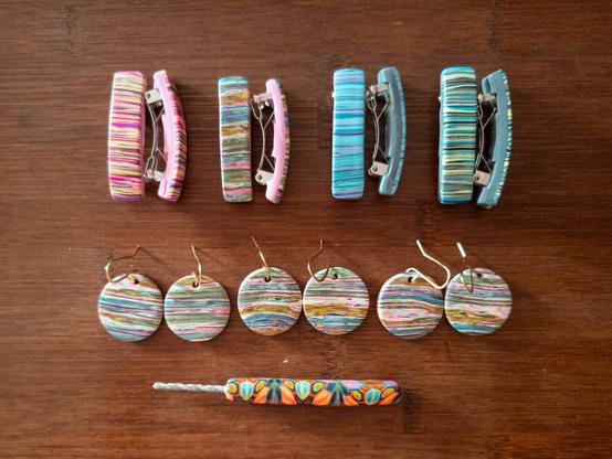 In the top row, four pairs of tiny barrettes, all with a "messy stripe" kind of pattern on them in different colors (pink, pastel multi, blue, and green). The next row has three pairs of earrings, with brass ear wires. The dangles are .75-inch circles in the pastel multi stripe design. In the bottom row is a drill bit with a polymer clay handle, in a rainbow-colored kaleidoscopic pattern.