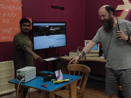 Two birkenhackers pointing at the 32x32 LED Pixel panel sitting on a table, gpredict is plotting satellites on a TV in the background