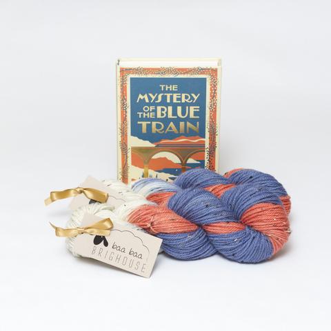 Picture shows two skeins of yarn in shades of blue, orange and white, positioned one behind the other. Behind the yarn, stood on its end, is a hardback copy of The Mystery of the Blue Train.