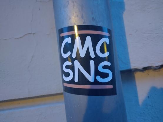 A Sticker with a black background, a red horizontal bar at the top and the bottom and in between the capital letters "CMC" and "SNS" underneath each other. The text and the bars are both in the Comic Sans font.