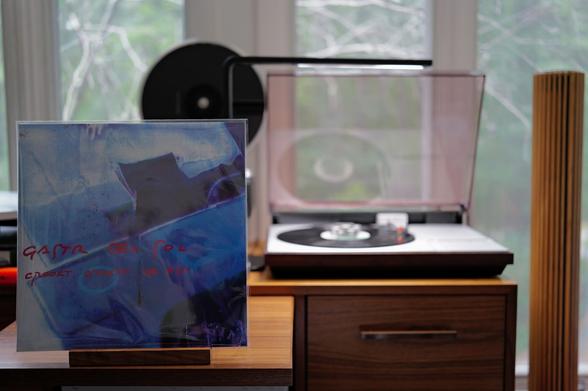 Gastr del Sol - Crookt, Crackt, or Fly LP cover.
A mostly blue picture of...something. The title is handwritten over in red.
The black LP plays on a vintage, restored Bang & Olufsen Beogram 4000 linear-tracking turntable to the right.