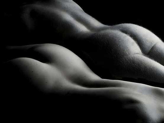 Klasssiche Aktfotografie in schwarzweiss mit Streiflicht.
Ein Paar liegt parallel zueinander nackt auf dem Bauch