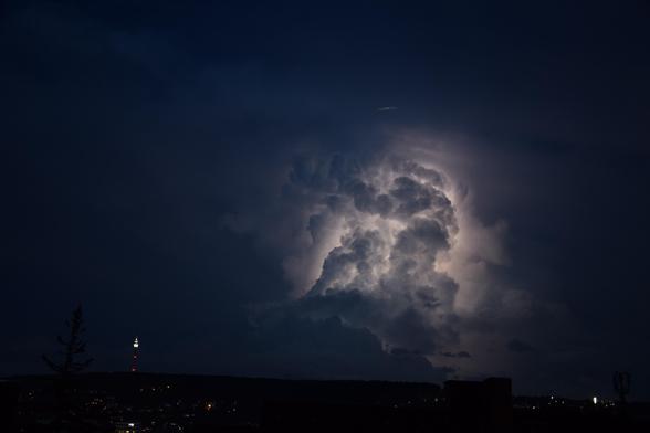 Die Gewitterwolke wird von hinten durch einen Blitz durchleuchtet. Links daneben sieht man den Stuttgarter Fernsehturm.