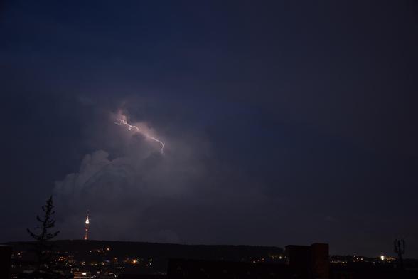 Ein rötlicher Blitz steigt aus der Wolke auf. Vor der Wolke sieht man die Dächer von Stuttgart und den Fernsehturm.