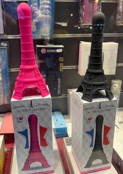 A pink and a black dildo, both in the shape of the Eiffel Tower, sit on their display boxes. The pink dildo on the left is slightly larger than the black dildo on the right. I do not own either of them.