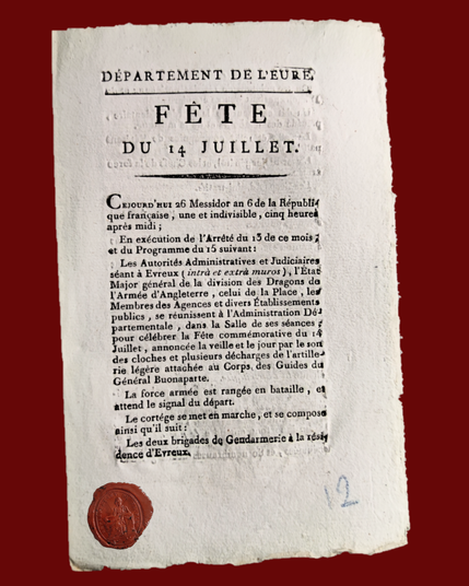 Photographie d'un document tapuscrit sur papier épais, il s'agit de la première page du compte-rendu des fêtes du 14 juillet. Un sceau républicain en cire rouge est rajouté sur l'image.