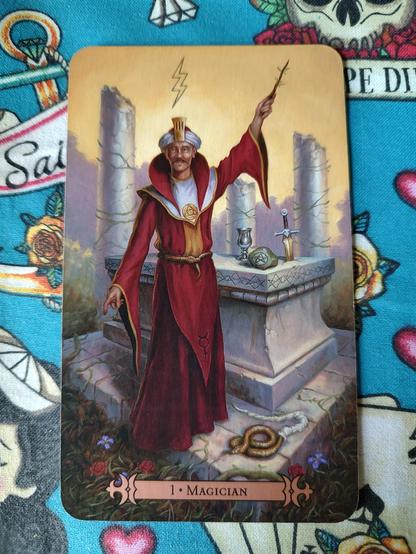 Card from the Modern Spellcaster's Tarot deck. 
The Magician-I.
A man in red robes, the magician, stands next to an altar. A hand points to the ground, his left hand points to the sky holding a wand. The altar has implements of his craft.