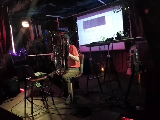 A man in an orange shirt, playing a tuba that hides his entire body
