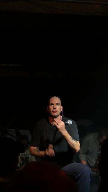 Mann mit Mikrofon in der Hand schaut genau in die Augen Kamera. Der Rest des Fotos sehr dunkel.