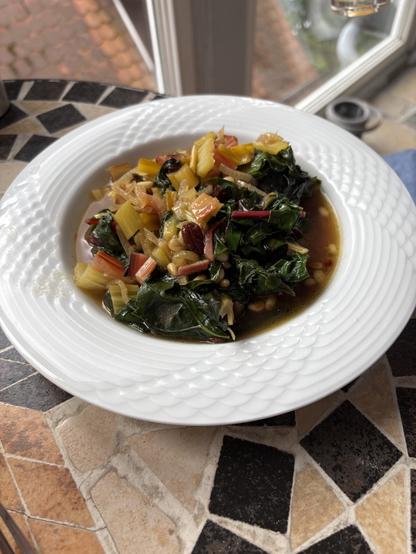 Weißer Teller auf Mossiktisch, gefüllt mit buntem Mangoldgericht