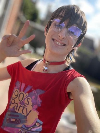 A selfie of me in an over-shoulder shirt, a bralette and a red bell choker. This photo was taken in my garden.