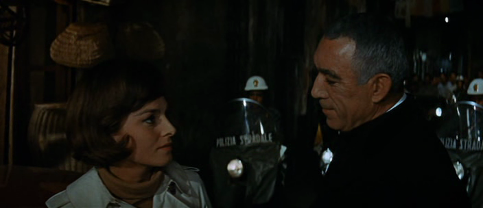 Consulta realizada correctamente

Una toma de primer plano de una mujer y un hombre, en una calle oscura, con oficiales de policía antidisturbios borrosos detrás de ellos. La mujer, a la izquierda, tiene el pelo castaño corto, una chaqueta blanca y una blusa de cuello alto. Está mirando al hombre. El hombre, a la derecha, está de perfil, mirando a la mujer. Tiene el pelo corto y oscuro y está vestido con un uniforme oscuro. Los oficiales de policía antidisturbios detrás de ellos llevan cascos blancos y escudos grandes y oscuros.